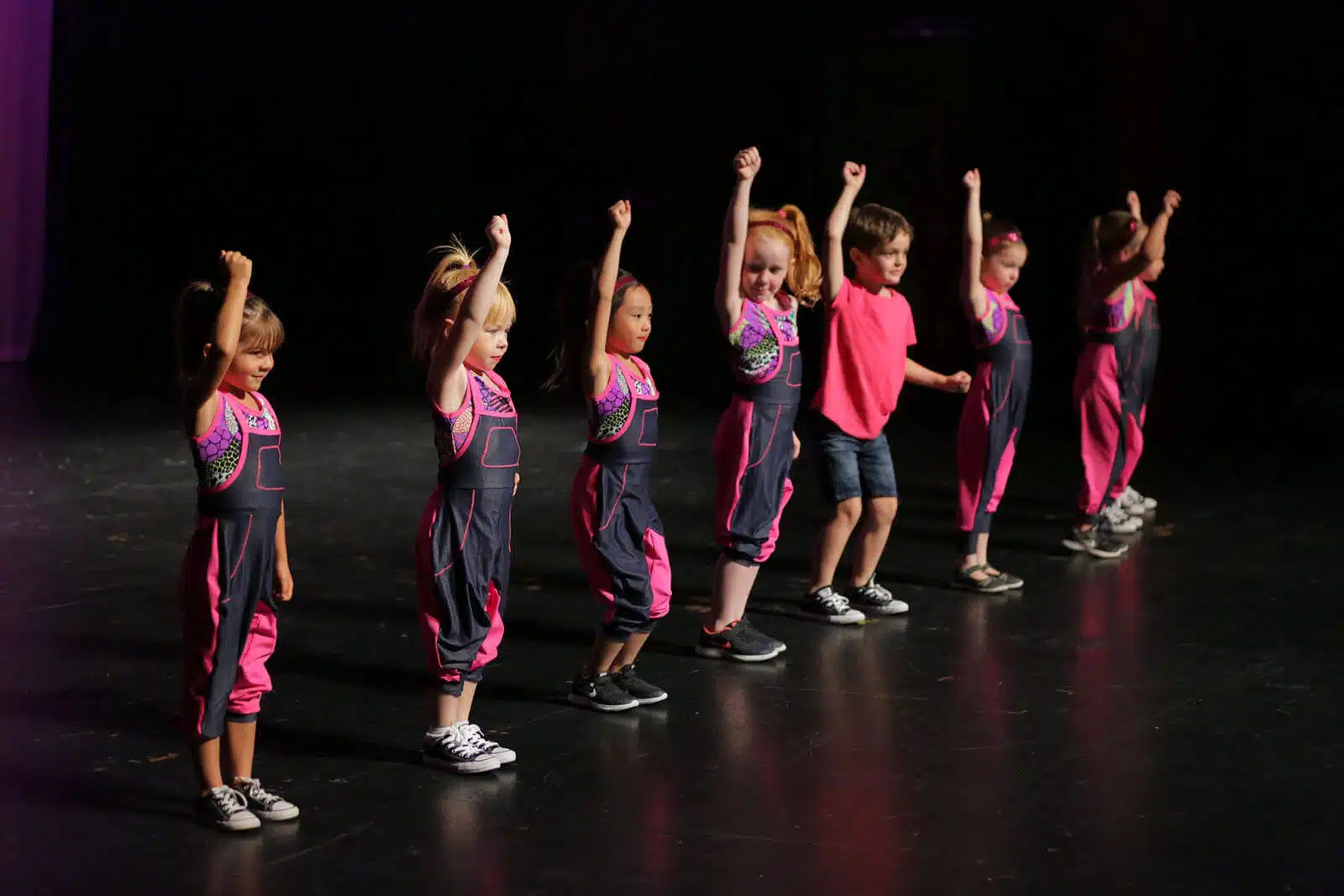 Dance Recital image. Group of young dancers in black and pink outfits performing on stage.